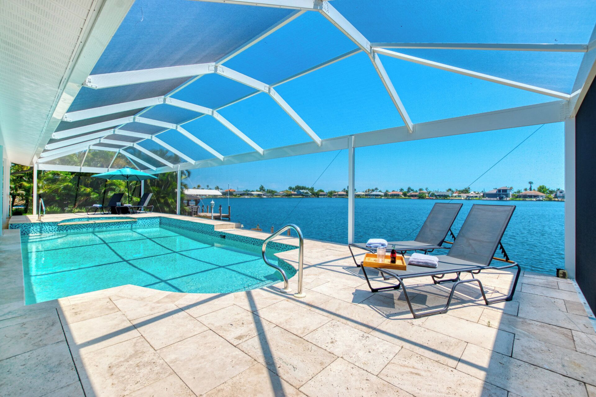 Un espace piscine offrant une vue dégagée sur l’eau, un coin salon couvert avec des chaises longues et une terrasse carrelée.