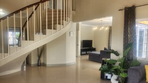 Un vaste espace de vie agrémenté d’un escalier en colimaçon, d’un téléviseur à écran plat et d’une grande plante.