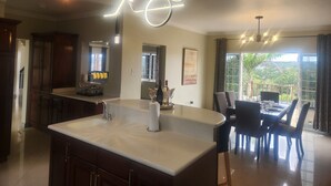 Une cuisine moderne dotée d’un îlot central, de luminaires suspendus et d’un coin repas offrant une vue sur l’extérieur.