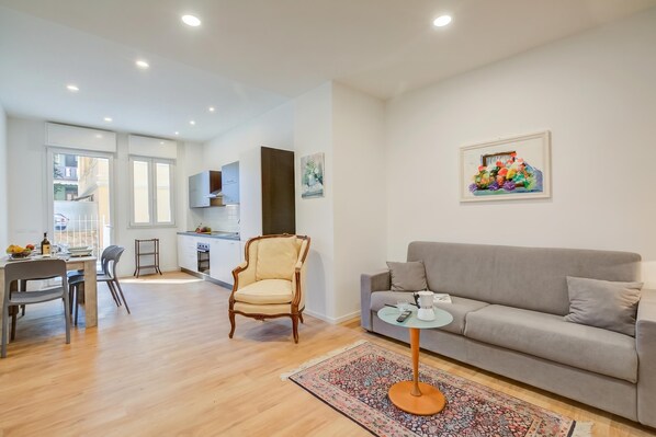 Un salon moderne avec un canapé gris, une chaise en bois, une petite table ronde et un tapis coloré.