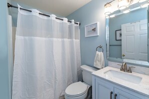 Une salle de bain avec un rideau de douche blanc, des toilettes, un lavabo avec un miroir et un porte-serviettes.