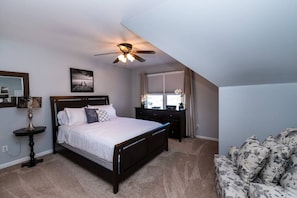 Une chambre à coucher avec un lit, un bureau, une chaise, un ventilateur de plafond et une fenêtre avec des rideaux.