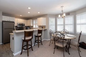 A kitchen with a refrigerator, microwave, and island with bar stools.