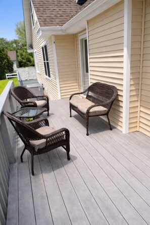 A deck with wicker furniture and a glass table.