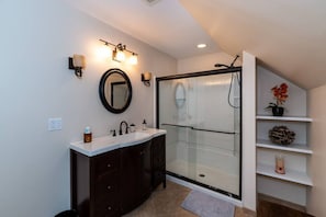 A modern bathroom with a glass shower enclosure, a vanity with dark wood cabinets, a round mirror, and wall-mounted sconces.