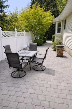 Une terrasse extérieure avec une table et des chaises, une clôture blanche et une maison en arrière-plan.