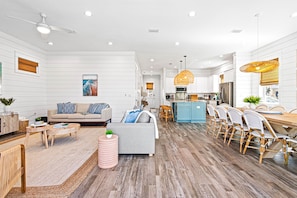 A spacious living area with a sofa, dining table, and chairs, a kitchen with modern appliances, and a ceiling fan.