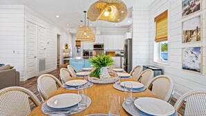 A dining area with a wooden table set for six, surrounded by wicker chairs, a central plant, and pendant lighting. - My Happy Place Miramar Beach - 6BR Villa, Private Pool and Hot Tub, Golf Cart (Miramar Beach)