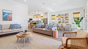 A spacious living area with a sofa, coffee table, and wicker chairs. A dining area with a table and chairs is visible in the background. - My Happy Place Miramar Beach - 6BR Villa, Private Pool and Hot Tub, Golf Cart (Miramar Beach)