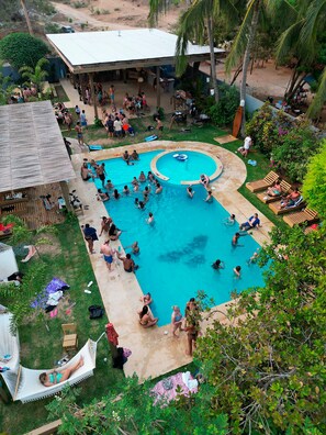 A large outdoor swimming pool surrounded by lounge chairs and a covered seating area. - Straw Hat Surf Hostel (Puerto Escondido)