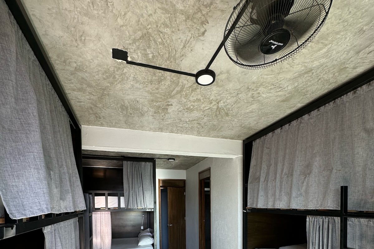 Habitación compacta y moderna con literas, ventilador de techo y una ventana pequeña que permite la entrada de luz natural.