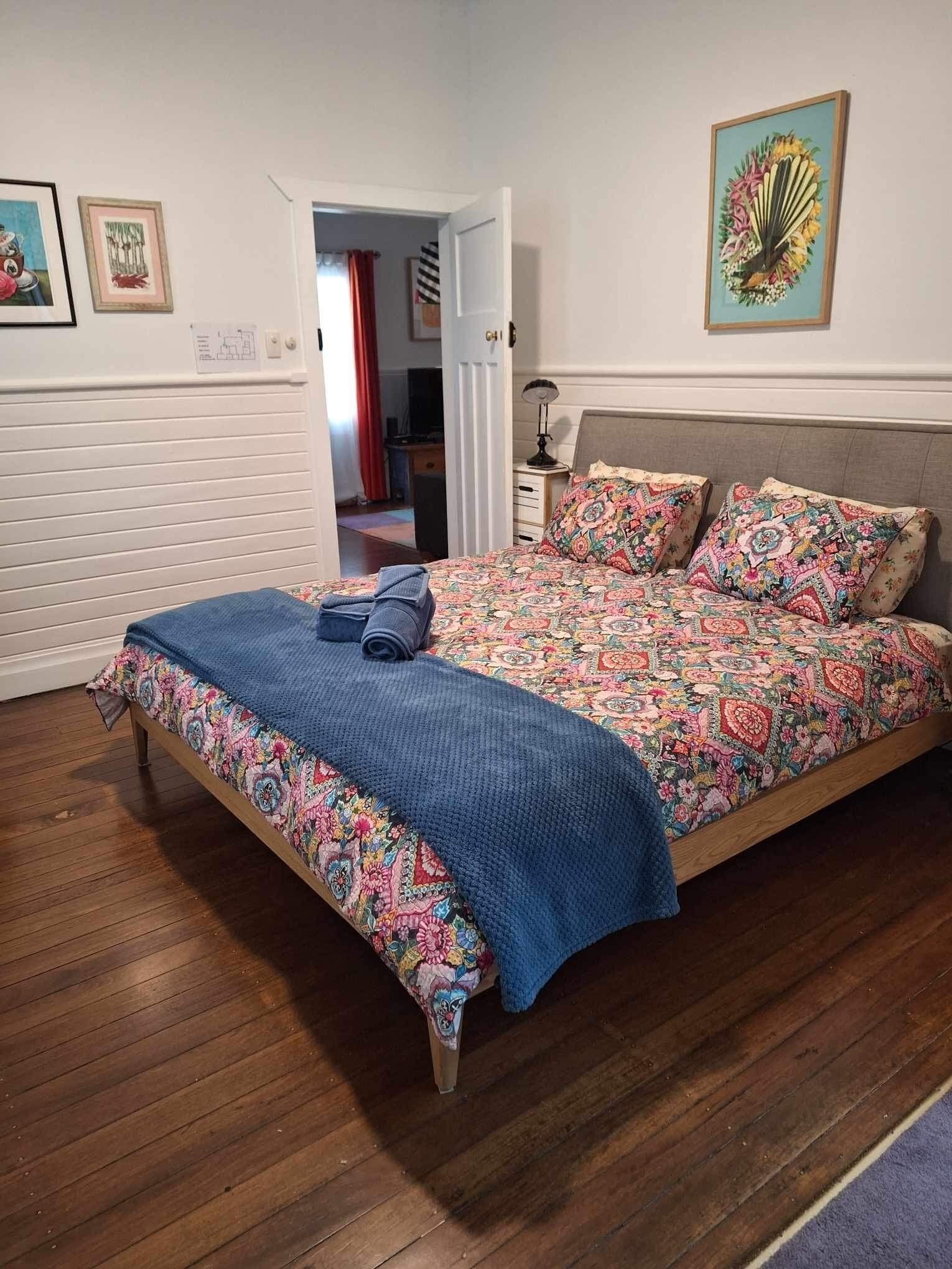A bedroom with a wooden bed, floral bedding, a blue blanket, and a door leading to another room.