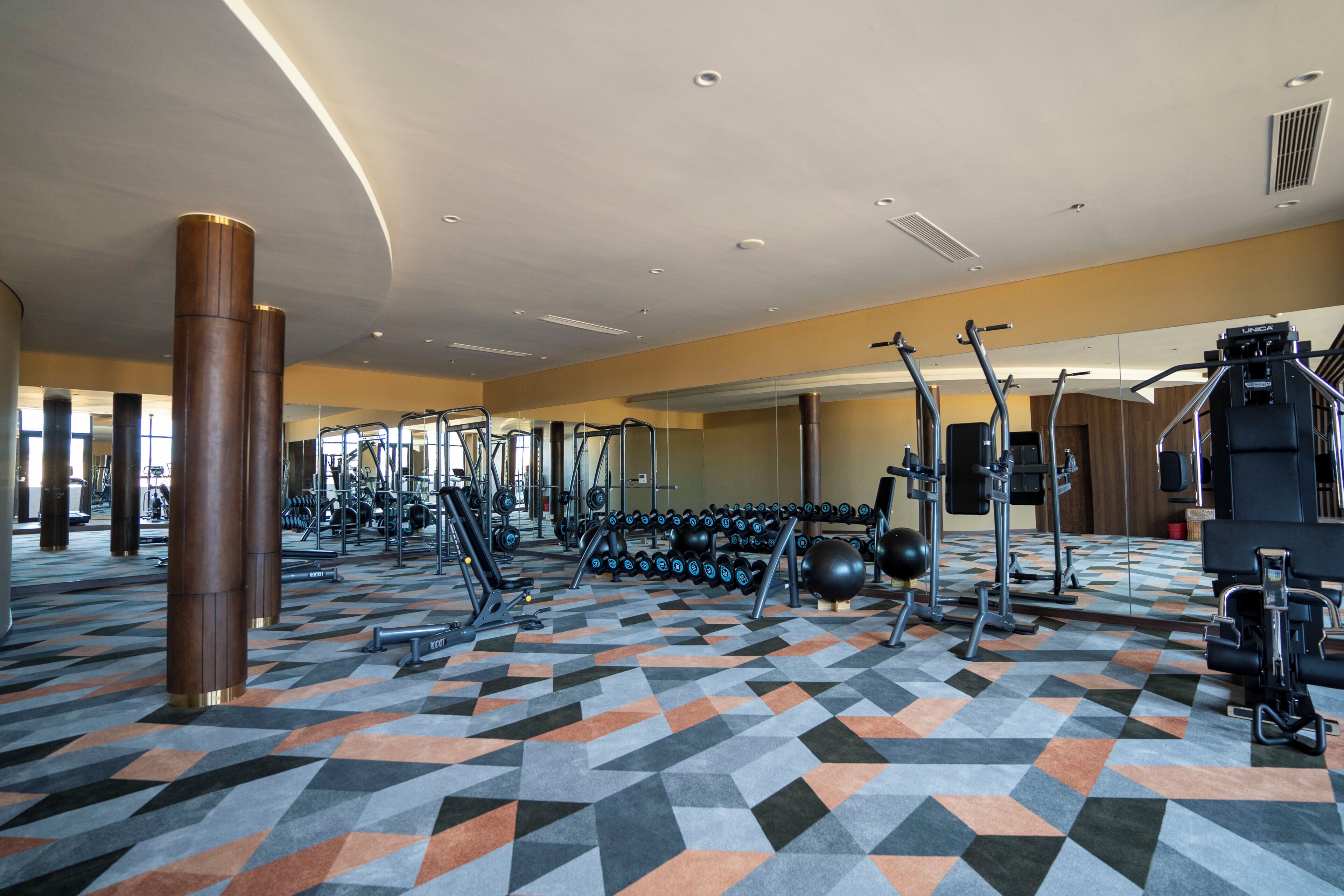 A gym with exercise equipment, a patterned floor, and large pillars.