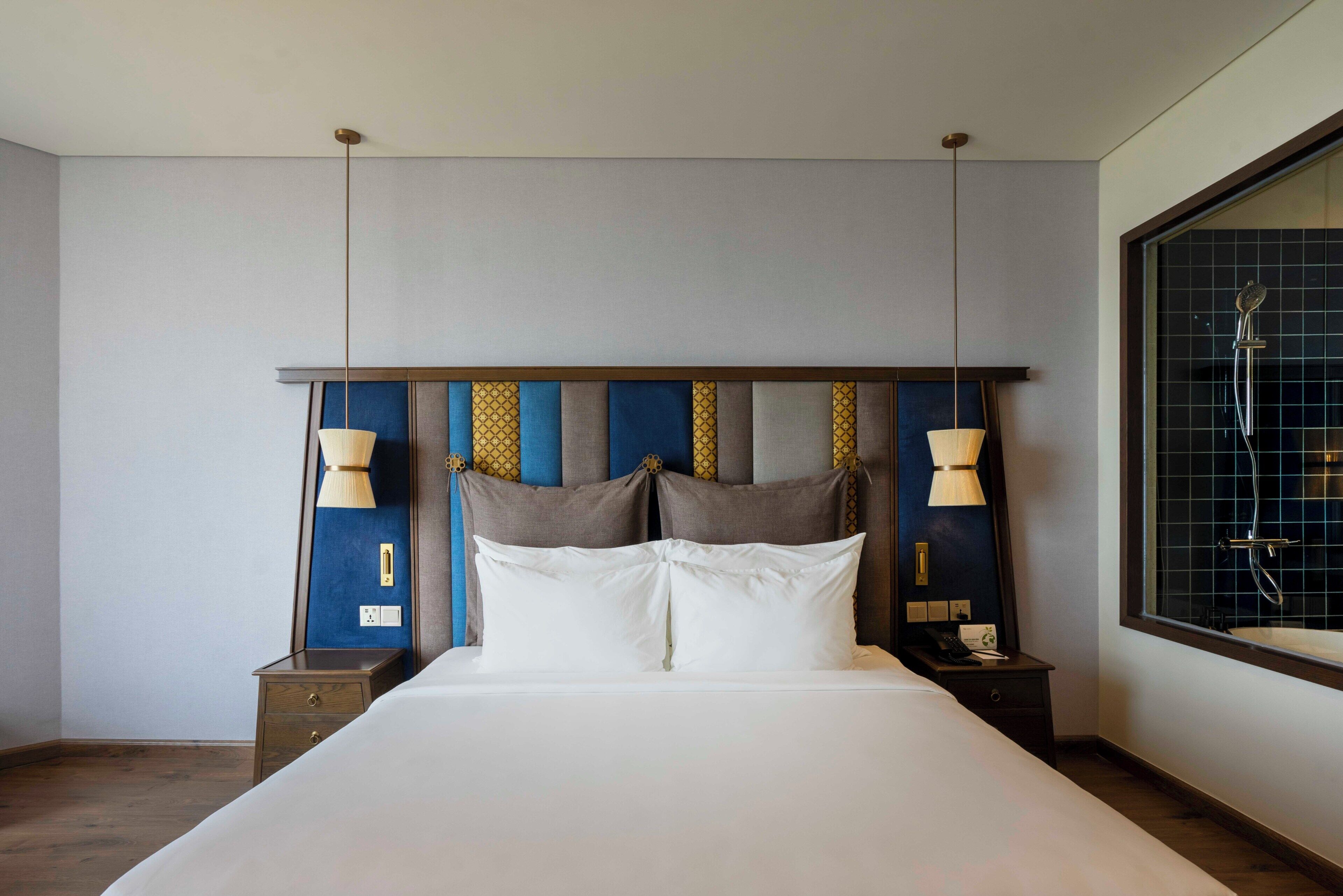 Een hotelkamer met een groot bed, twee nachtkastjes, een raam met uitzicht op een betegelde muur en een douche.