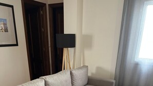 En grå hörnsoffa i ett rum med ett kaklat golv, en inramad tavla på väggen och en golvlampa.