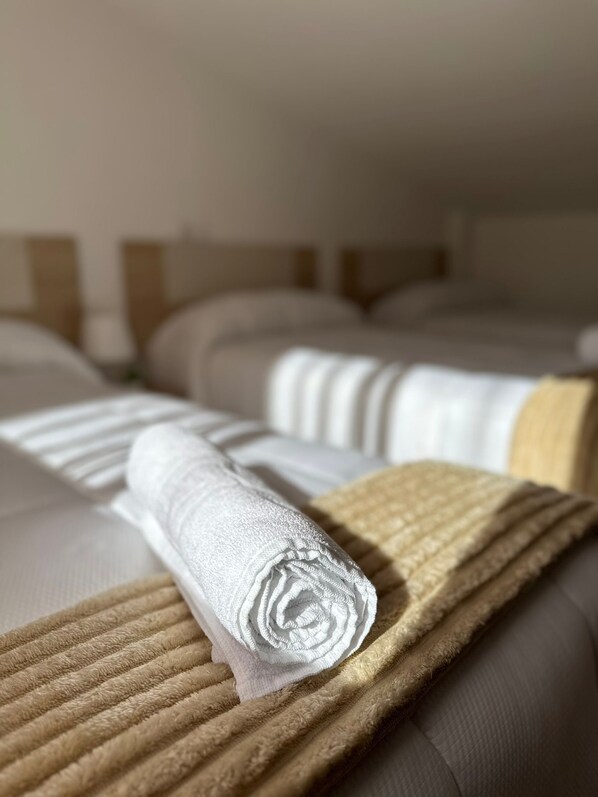 Habitación de hotel con dos camas, cada una con una colcha blanca y una manta color arena.