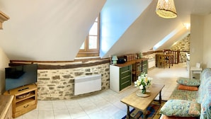 Una habitación acogedora en el desván con pared de piedra, un mueble de madera para entretenimiento, un televisor, una mesa de comedor con sillas y un sofá.