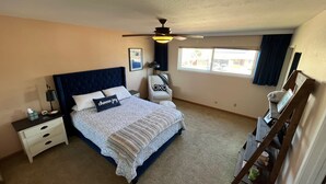 A bedroom with a bed, nightstands, a desk, a chair, a ceiling fan, and a window.