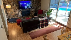 A living room with a stone wall, a flat-screen TV, a fireplace, a sofa, a coffee table, and a view of a swimming pool.