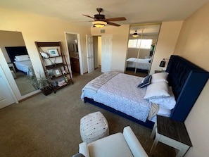 Une chambre à coucher comprenant un lit, un ventilateur de plafond, une bibliothèque, un miroir et une porte donnant sur une autre pièce.