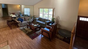 A spacious living room with a high ceiling, a staircase leading to an upper level, and a large window providing natural light.