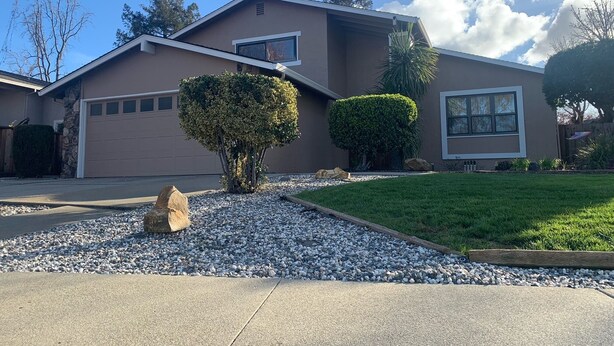 A modern two-story house with a garage, two well-maintained hedges, and a gravel driveway.