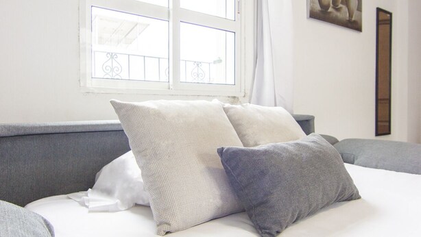 Uma cama bem arrumada com duas almofadas, uma janela com vista e um quadro na parede.