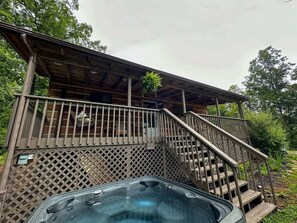 Une cabane en bois avec un jacuzzi, un escalier et une terrasse couverte.