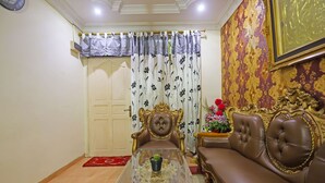 A living room with a glass coffee table, a brown leather sofa, a decorative chair, and a curtain with floral patterns. - Hotel O Satria Homestay Syariah (Batam)