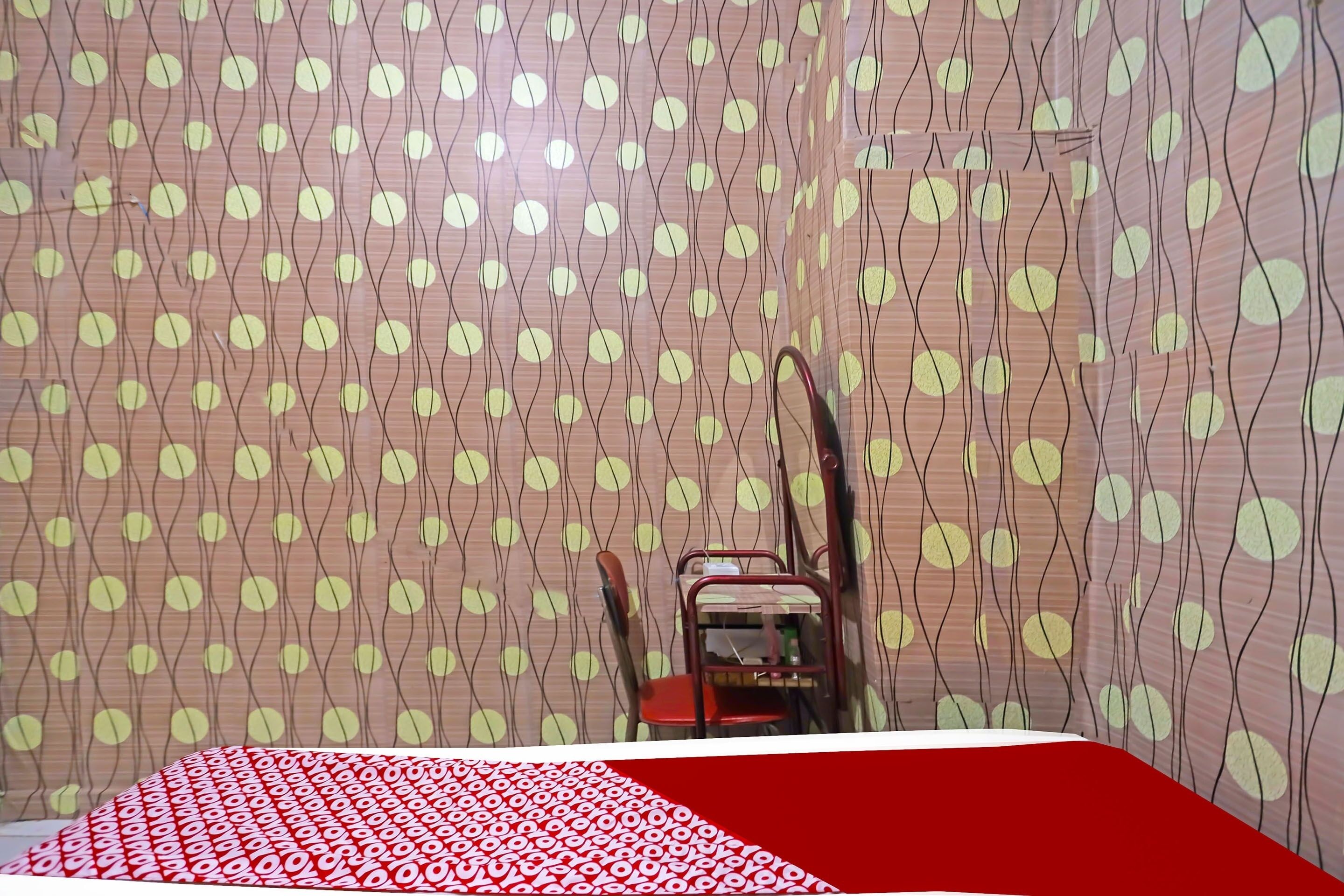 A room with a patterned wallpaper, a red and white bedspread, and a chair with a red cushion.