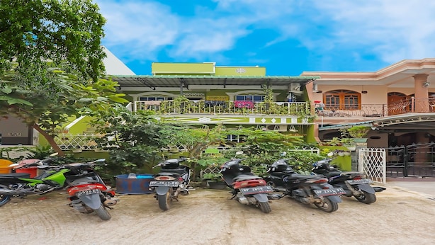 A multi-story building with a green and pink facade, a covered balcony, and several parked scooters. - Hotel O Satria Homestay Syariah (Batam)