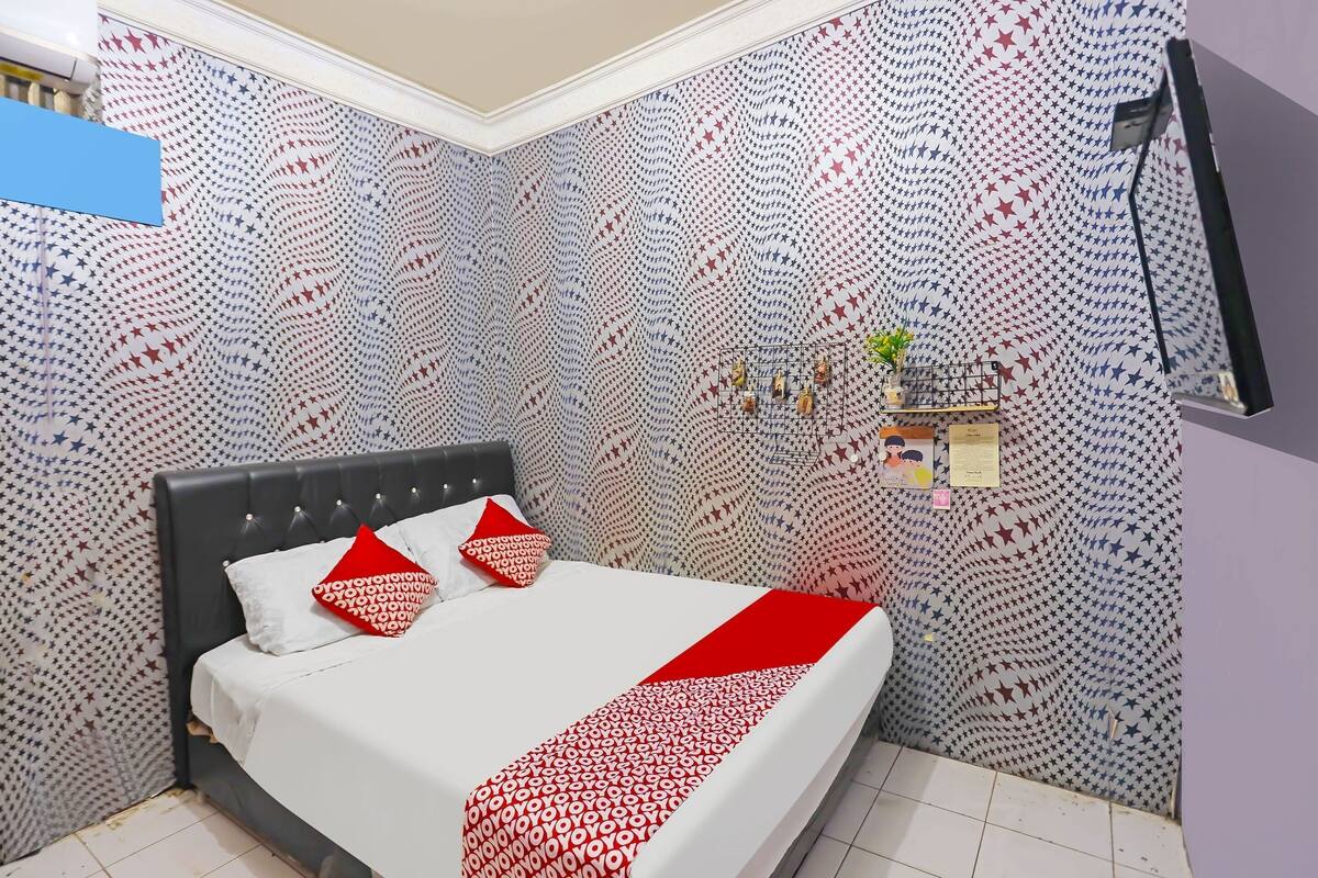 Een keurig opgemaakt bed met een patroon op de muur en een kleine plant op een plank.