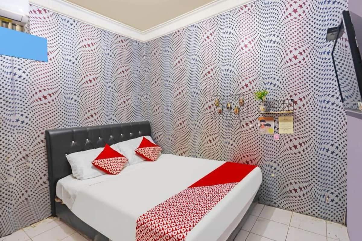 Een slaapkamer met een bed, behang met een patroon, een klein plantje en een tv aan de muur.