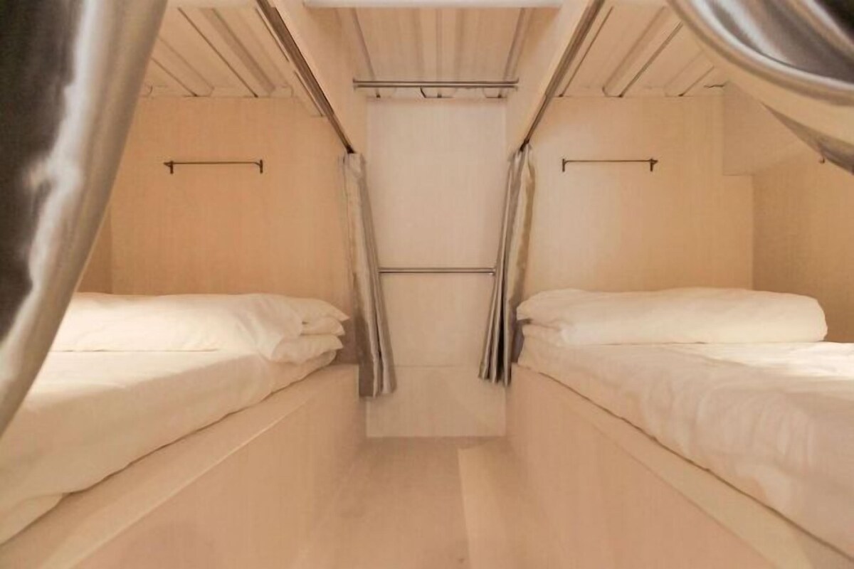A compact, single-room hotel with two beds, a wooden ceiling, and a central window.