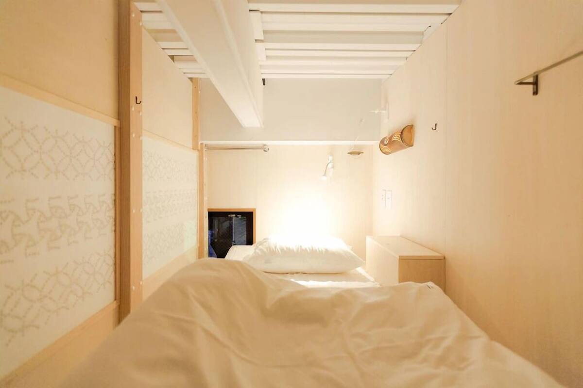 A bedroom with a bed, a bedside table, a wall-mounted shelf, and a small window.