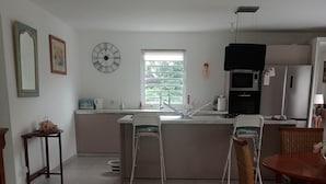 Cozinha moderna com ilha central, área de refeições com cadeiras de vime e um relógio na parede.