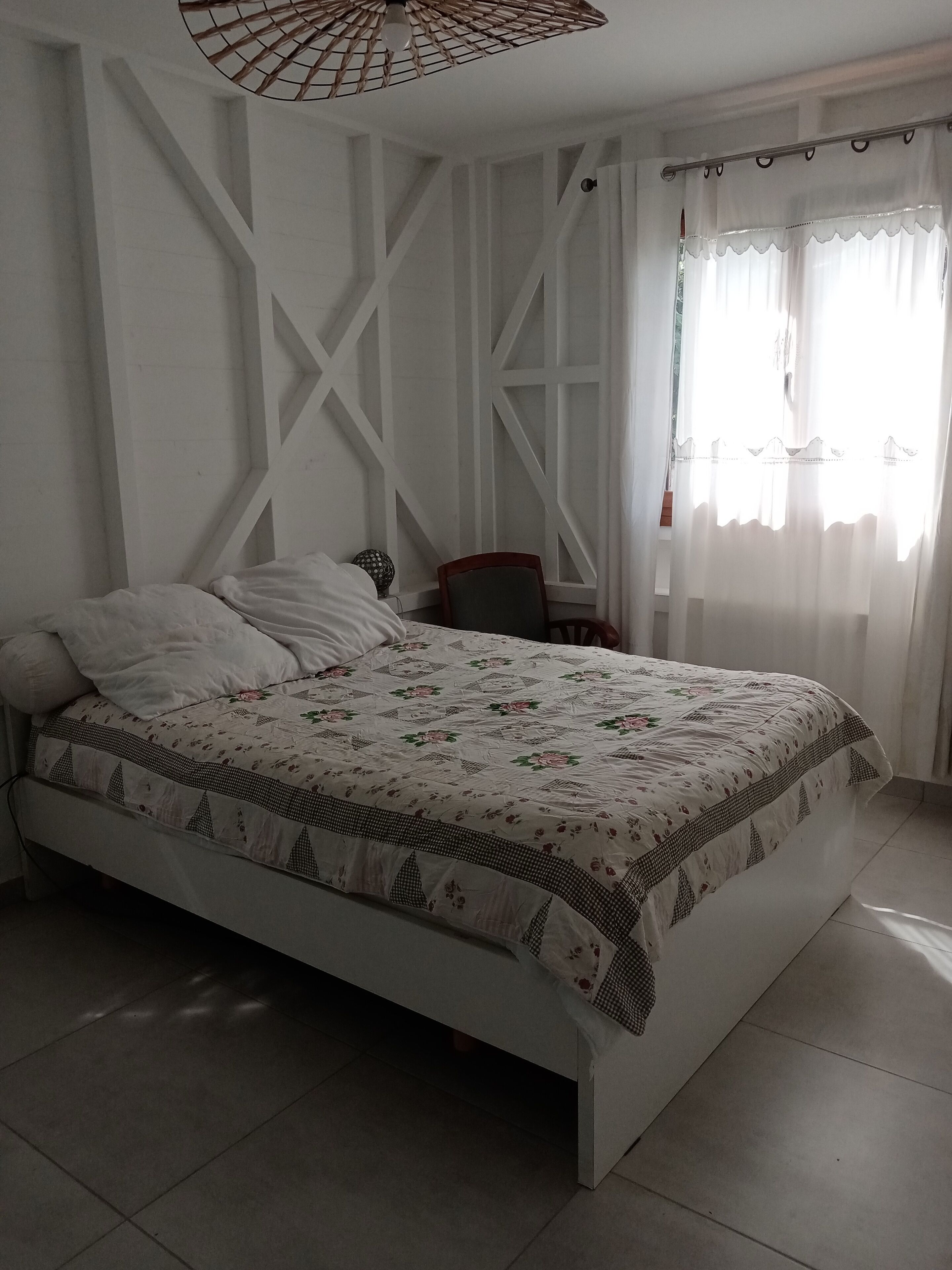 A bedroom with a bed, a chair, a lamp, and a window with curtains.