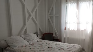 Quarto com cama, cadeira, abajur e janela com cortinas.