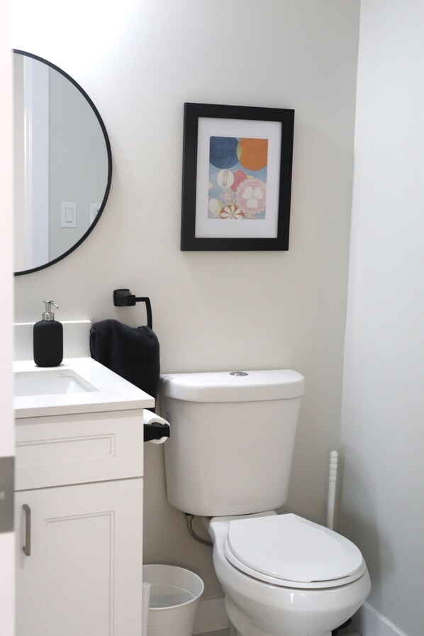 A bathroom with a toilet, sink, and a framed picture on the wall. - Rare*Full Home in Downtown Winnipeg|Free Parking (Winnipeg)
