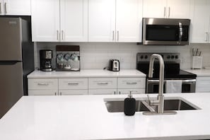 A modern kitchen with white cabinets, a stainless steel refrigerator, a coffee maker, a toaster, a microwave, and a sink with a faucet.