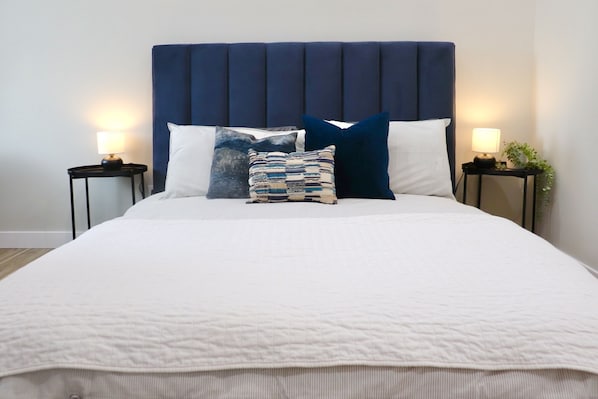 A bed with a dark headboard, white bedding, and two bedside tables with lamps.