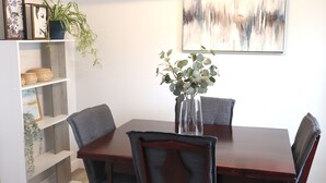 A dining area with a wooden table, four grey upholstered chairs, a vase with green foliage, and a wall-mounted abstract painting. - Rare*Full Home in Downtown Winnipeg|Free Parking (Winnipeg)