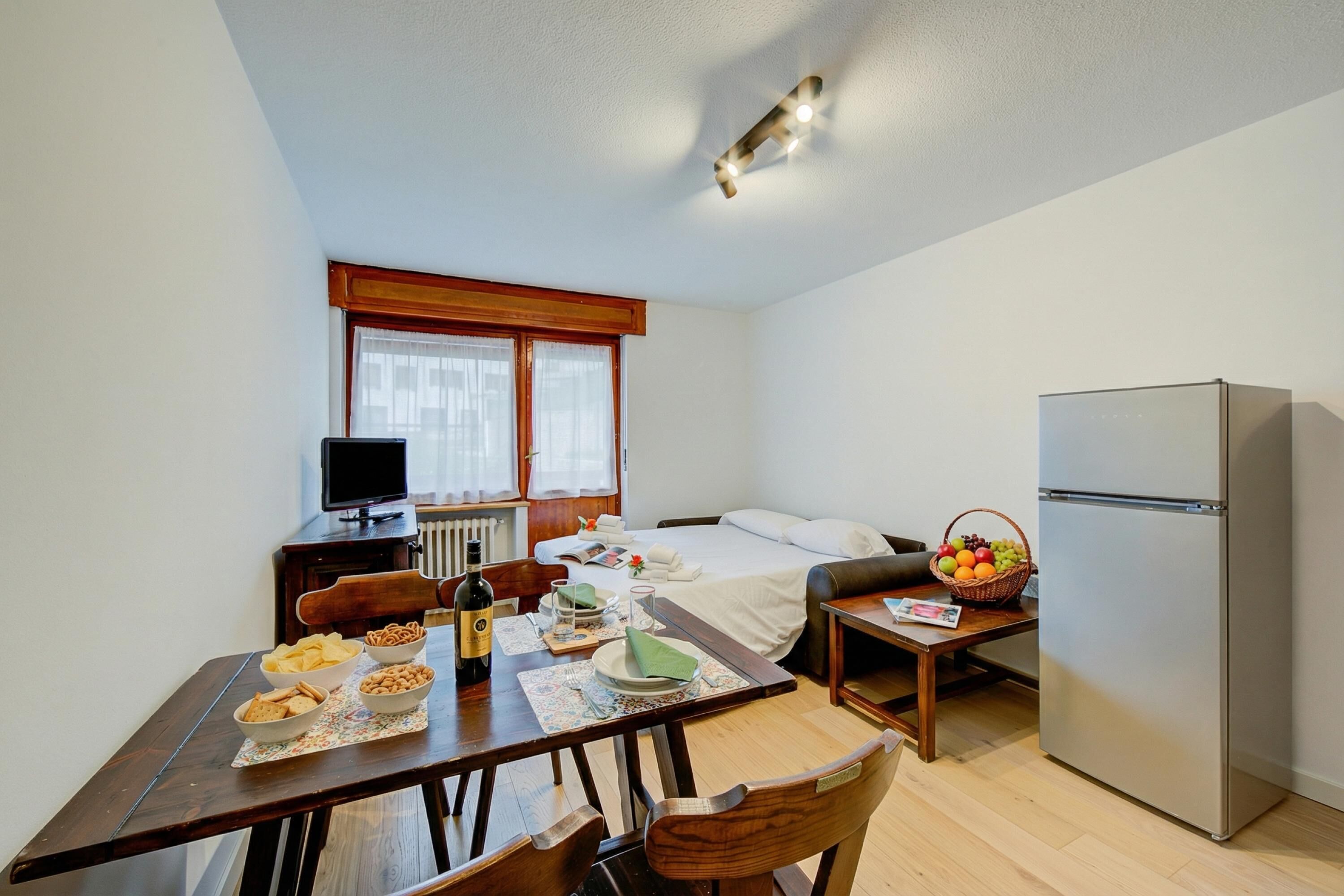 Une chambre de taille modeste comprenant un lit, une petite table à manger avec quelques collations, un réfrigérateur et un téléviseur.