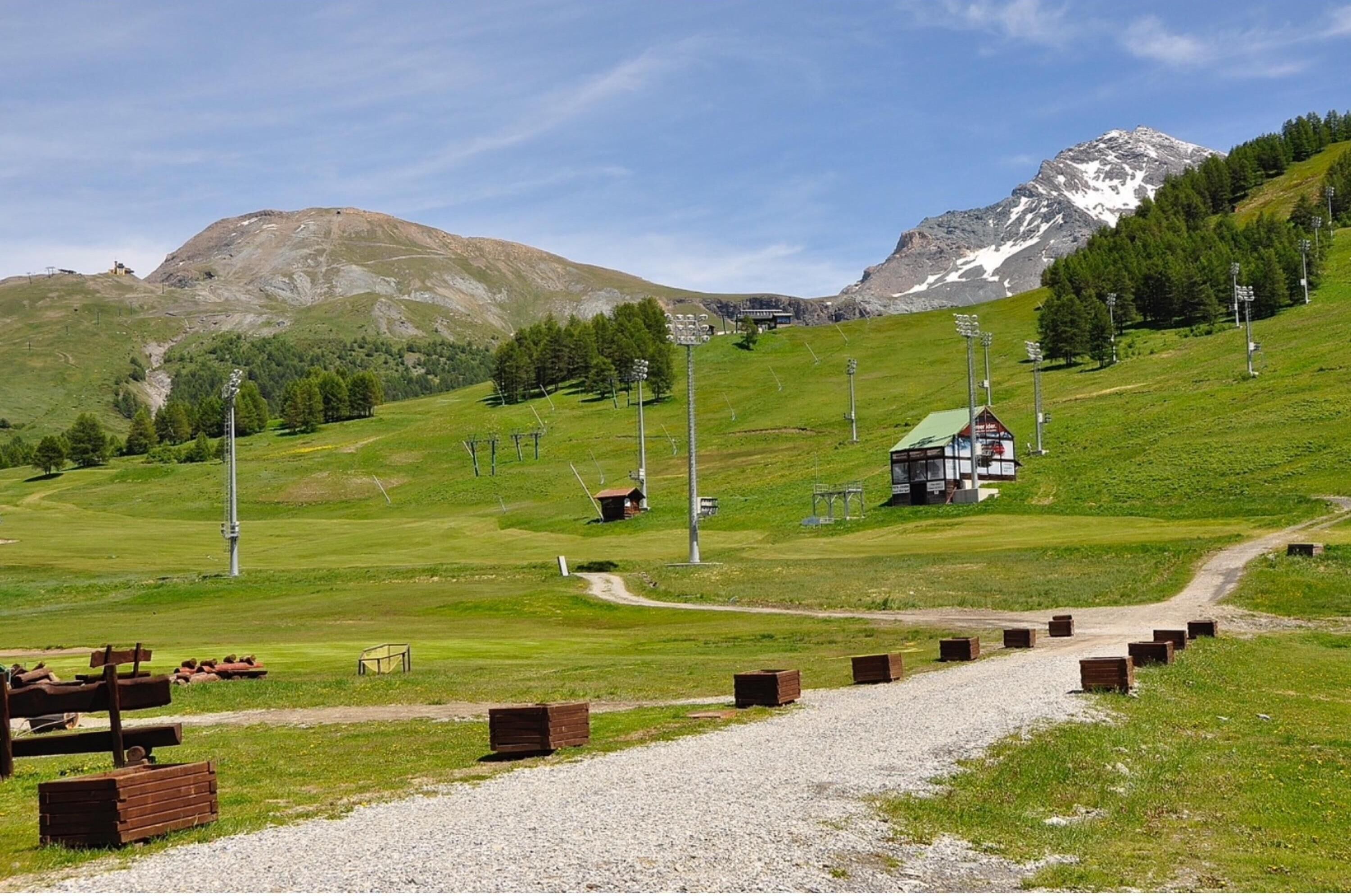 A mountain landscape with a small building, a gravel path, and wooden structures.