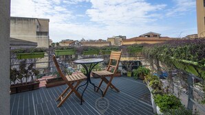 A rooftop terrace with two wooden chairs and a table, surrounded by potted plants and a view of the cityscape. - Tania's House - Wonderful Oristano (Oristano)