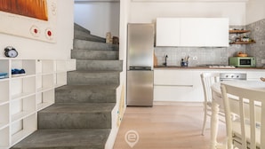 A modern kitchen with white cabinets, a stainless steel refrigerator, and a microwave. There is a staircase with a concrete finish leading to another level. - Tania's House - Wonderful Oristano (Oristano)