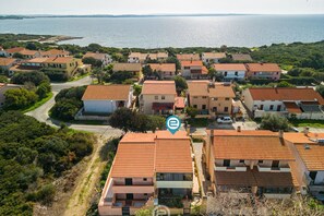 A coastal residential area with terracotta-roofed houses, a clear view of the sea, and a winding road.