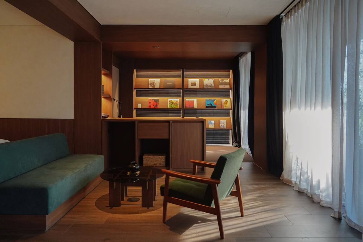 A modern living room with a sofa, armchair, and coffee table. A bookshelf with framed pictures is in the background.