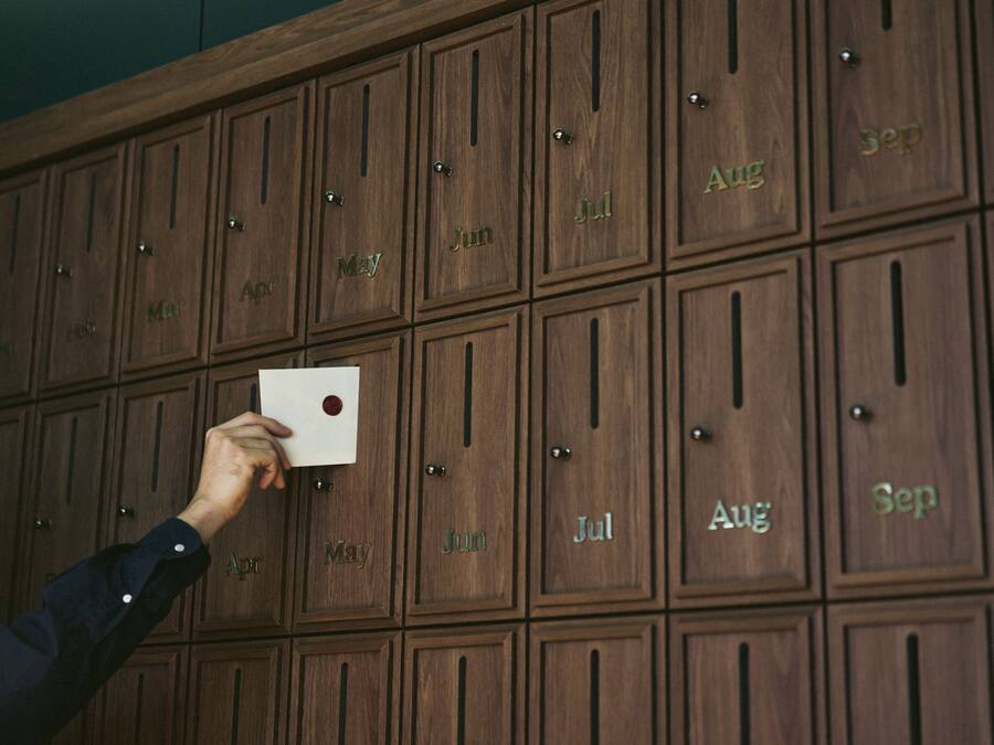 A hand holding a card in front of a wall of wooden lockers with months labeled on them.