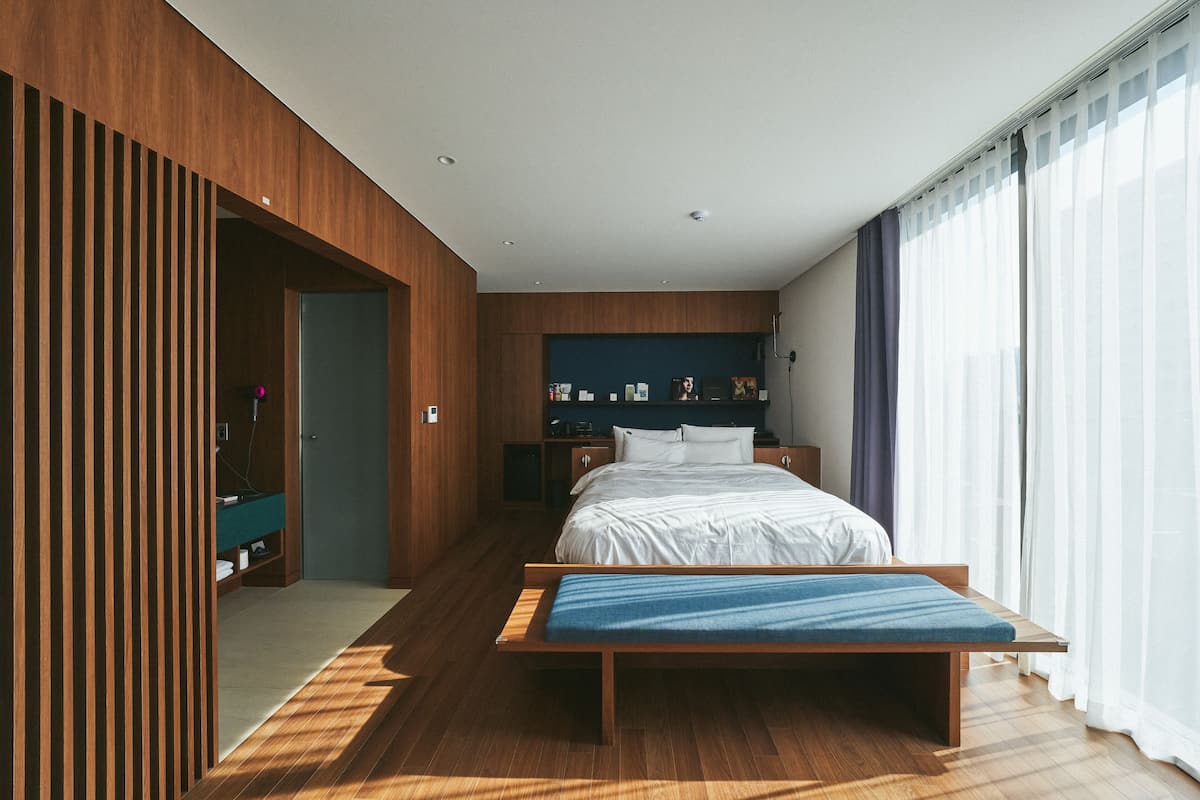 A modern bedroom with a wooden floor, a bed with a blue bench, a nightstand, and a wardrobe.